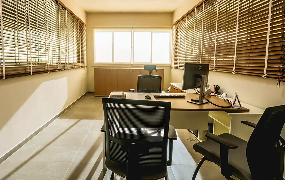 Sala de atendimento com mesas de escritório e mesa executiva, iluminada pelo sol.
